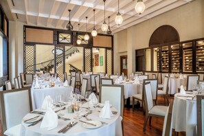 Un restaurant avec de nombreuses tables dressées pour le service, un escalier en arrière-plan et une cave à vin visible à travers une cloison vitrée.