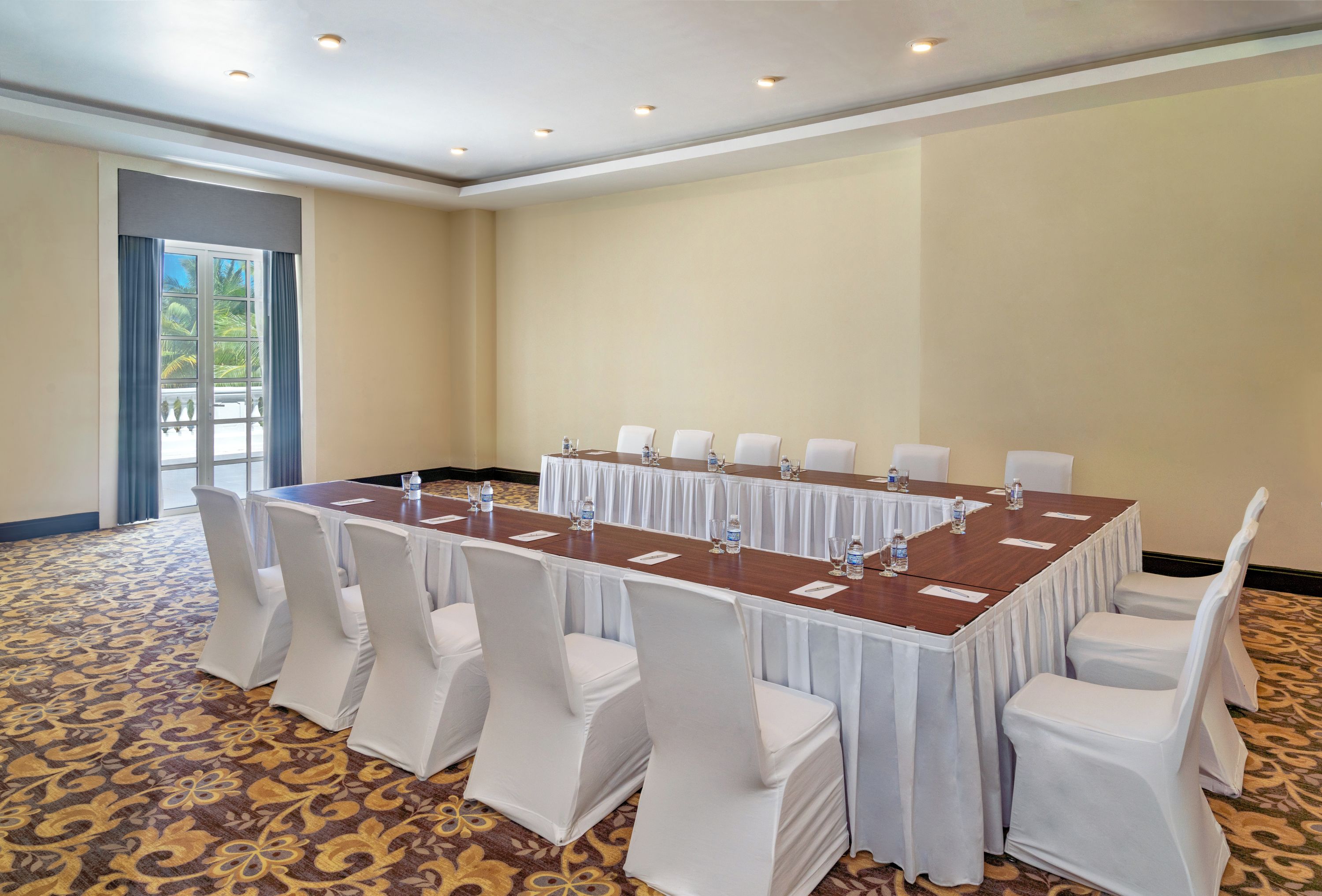 A conference room with a long table, white chairs, and a patterned carpet.