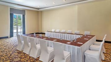 A conference room with a long table, white chairs, and a patterned carpet.