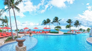 A pool with red umbrellas and lounge chairs, surrounded by palm trees and a clear sky.