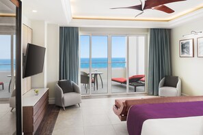 A hotel room with a bed, a desk, a TV, a balcony with a view of the sea, and two chairs. - Jewel Grande Montego Bay Resort&spa (Montego Bay)