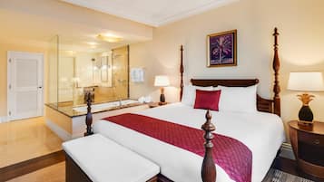 A hotel room with a large bed, a separate sitting area, a bathroom with a glass shower enclosure, and a large mirror.