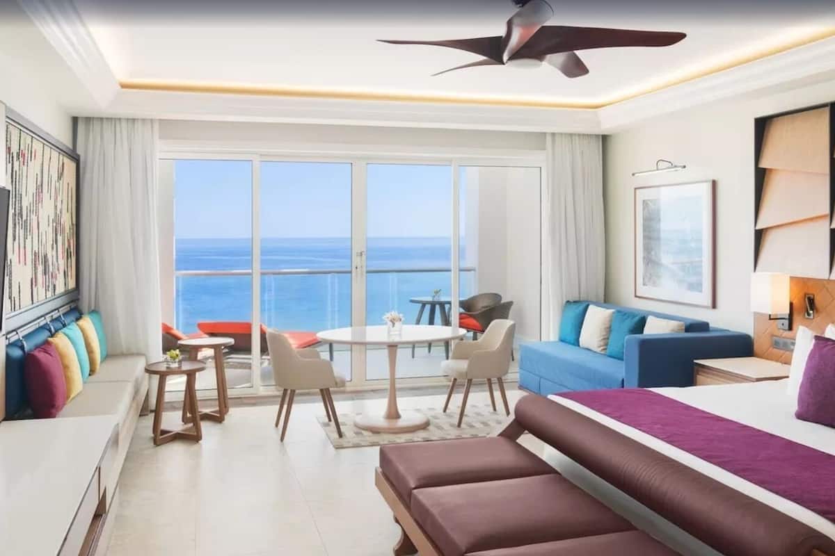 Una habitación de hotel moderna con balcón, cama, sofá, mesa de comedor y televisión.