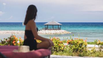 A person sitting on a chair with a view of the ocean and a gazebo on a rocky outcrop.