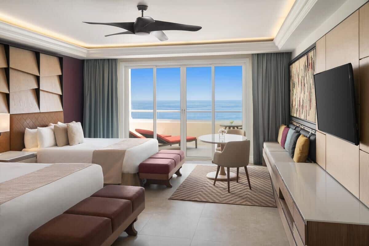 Habitación de hotel con cama, zona de estar, televisión y vista al océano.
