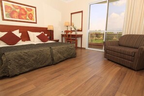 A hotel room with a large bed, a wooden desk, a chair, and a balcony with a view. - Pastoral Hotel (HaGalil HaElyon)