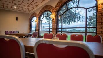 A conference room with a long table and red chairs, large arched windows, and a brick wall.