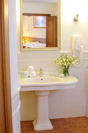 A bathroom with a pedestal sink, a mirror, a vase of flowers, and a hand sanitizer dispenser. - Pastoral Hotel (HaGalil HaElyon)