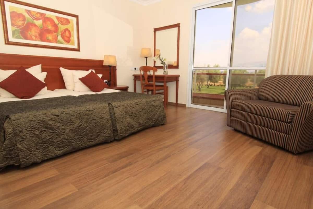 Habitación de hotel con una cama grande, un escritorio de madera, una silla y un balcón con vistas.