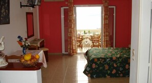 Quarto com cama, escrivaninha com um vaso de flores e uma mesa com frutas.