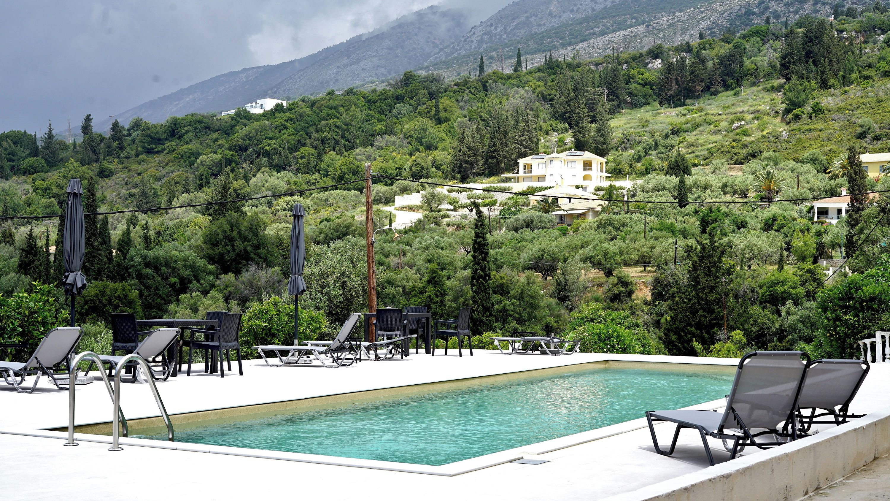 A pool area with lounge chairs and a view of a mountainous landscape.