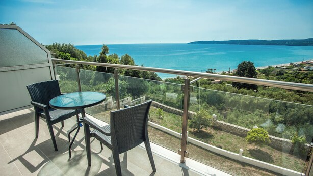 Un balcón con barandilla de vidrio que ofrece una vista panorámica del mar y la vegetación.