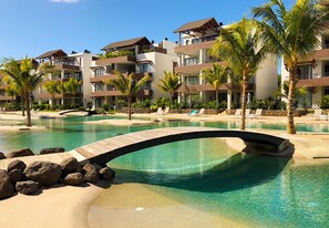 Ein Resort mit klarem Pool, einer Holzbrücke und mehrstöckigen Gebäuden mit Balkonen.