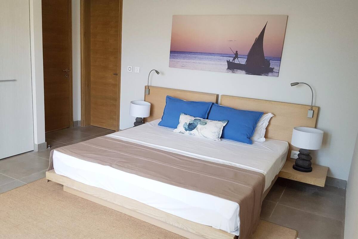 Un dormitorio con una cama, dos lámparas de noche, un cuadro de un velero y una puerta de madera.