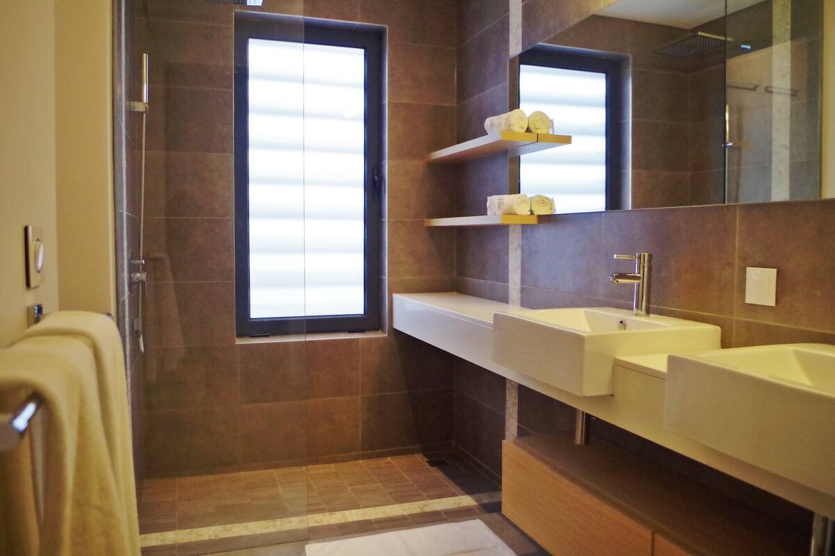Un baño con un ventanal grande, dos lavamanos y un espejo.