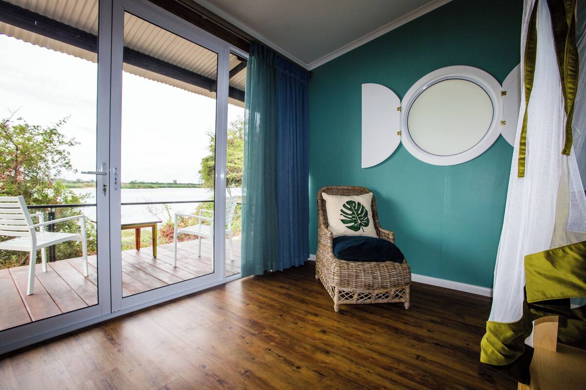 Una habitación con una silla de mimbre, un espejo grande y vistas a un balcón con mobiliario exterior.
