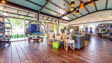 Una habitación amplia con piso de madera, una zona de estar con sofá y sillones, un expositor circular de zapatos y un ventanal que proporciona luz natural.