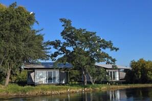 A lakeside property with two modern cabins, one with a glass facade and the other with a metal roof, surrounded by trees and a calm water body.