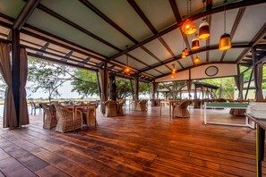 An outdoor covered dining area with wooden flooring, wicker furniture, and hanging pendant lights.