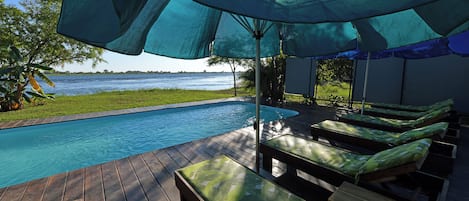 Un área junto a la piscina con sillones de descanso y una sombrilla grande.
