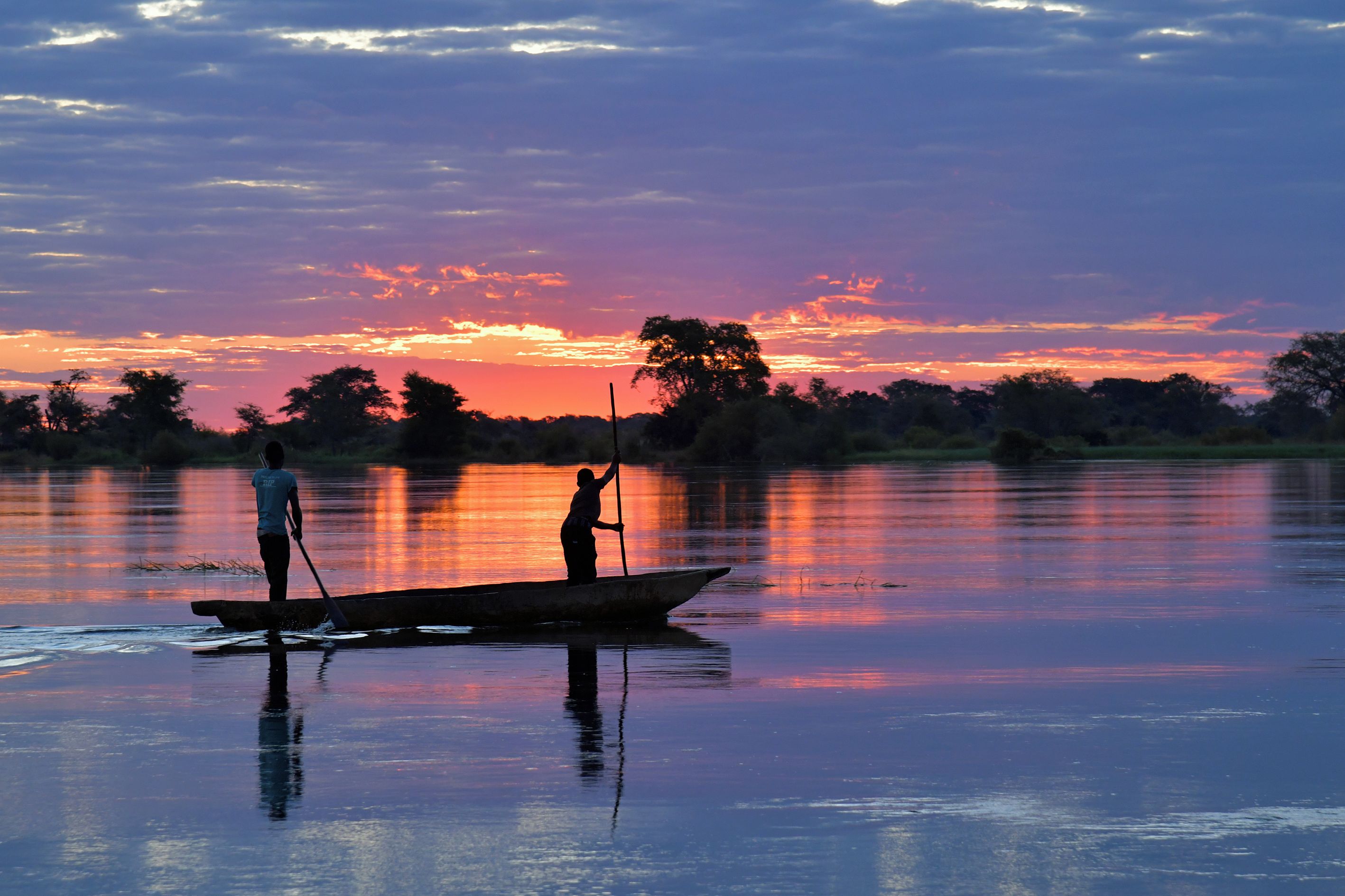 Un cuerpo de agua tranquilo con dos personas en un bote, rodeado de árboles y un cielo al atardecer.