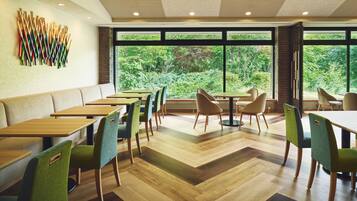A modern dining area with wooden tables and chairs, large windows with a view of greenery, and a unique wall art installation.