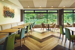 A modern dining area with wooden tables and chairs, large windows with a view of greenery, and a unique wall art installation. - ANA Holiday Inn Resort Karuizawa by IHG (Naganohara)