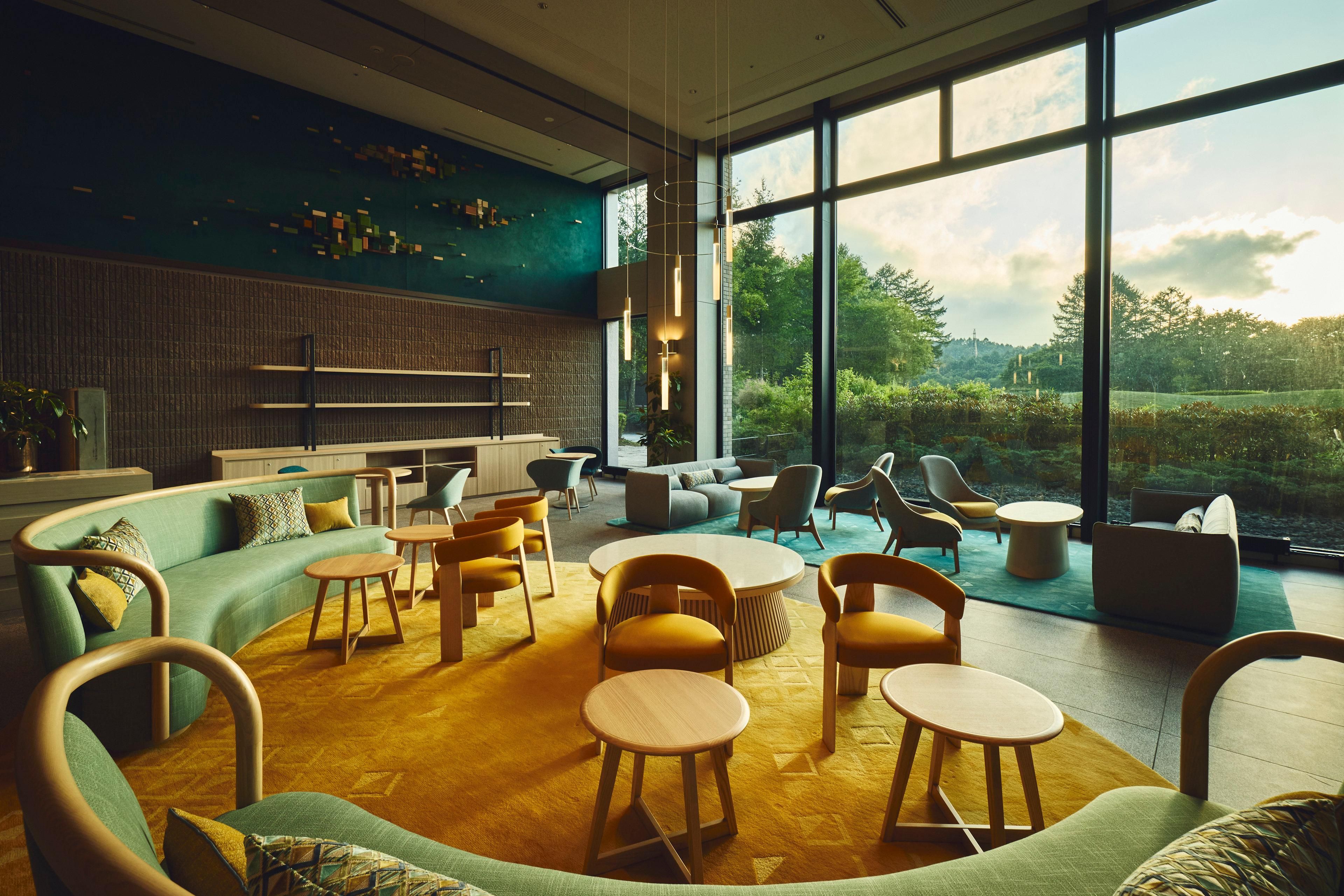 A modern interior with a curved sofa, round wooden tables, and a view of greenery outside.