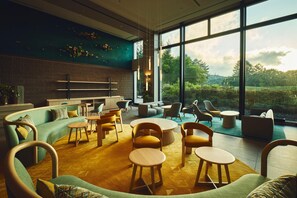 A modern interior with a curved sofa, round wooden tables, and a view of greenery outside. - ANA Holiday Inn Resort Karuizawa by IHG (Naganohara)