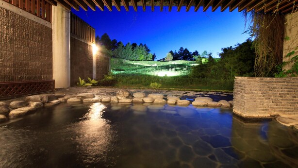 Un jacuzzi de piedra con una cubierta de madera, rodeado por un muro de piedra y una estructura de ladrillo.