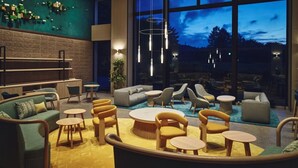 Un área de descanso moderna con sofás, sillas y mesas, ventanas amplias con vistas al exterior e iluminación colgante.