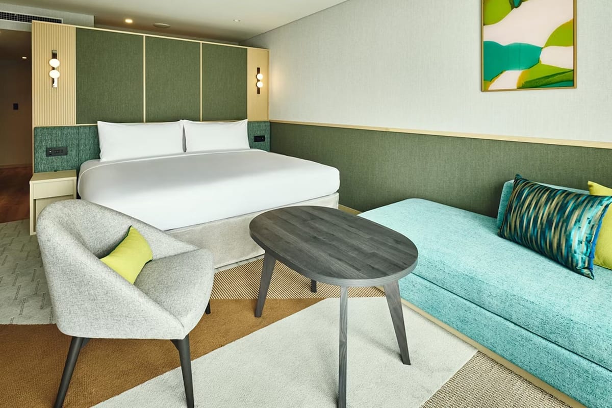 Hotellihuone, jossa on sänky, sohva, pieni pöytä ja tuoli.
