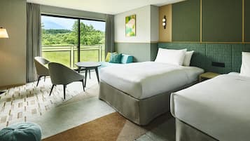 A hotel room with two beds, a sofa, a table, and a view of a green landscape.