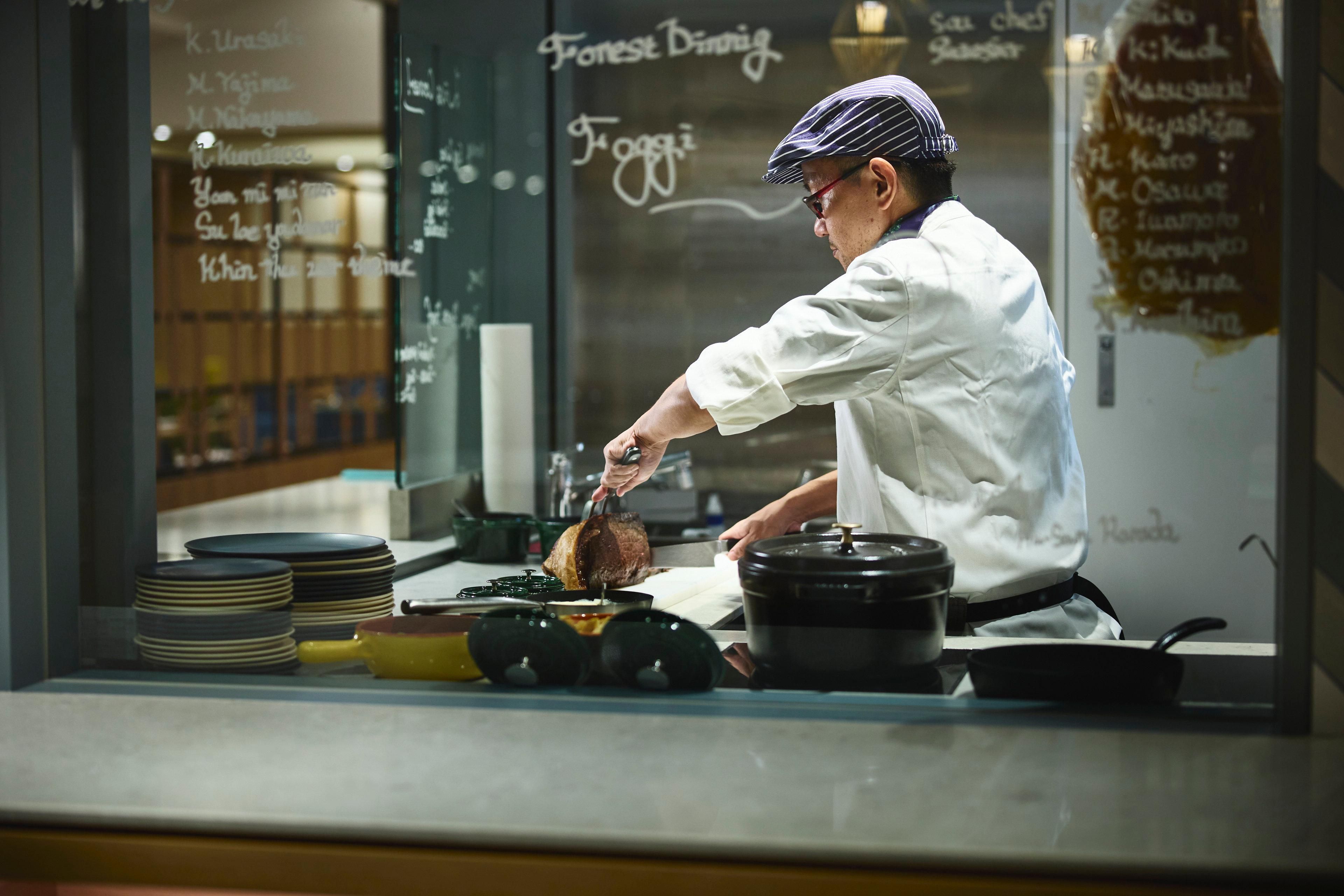 A chef preparing food in a kitchen with a chalkboard menu in the background.