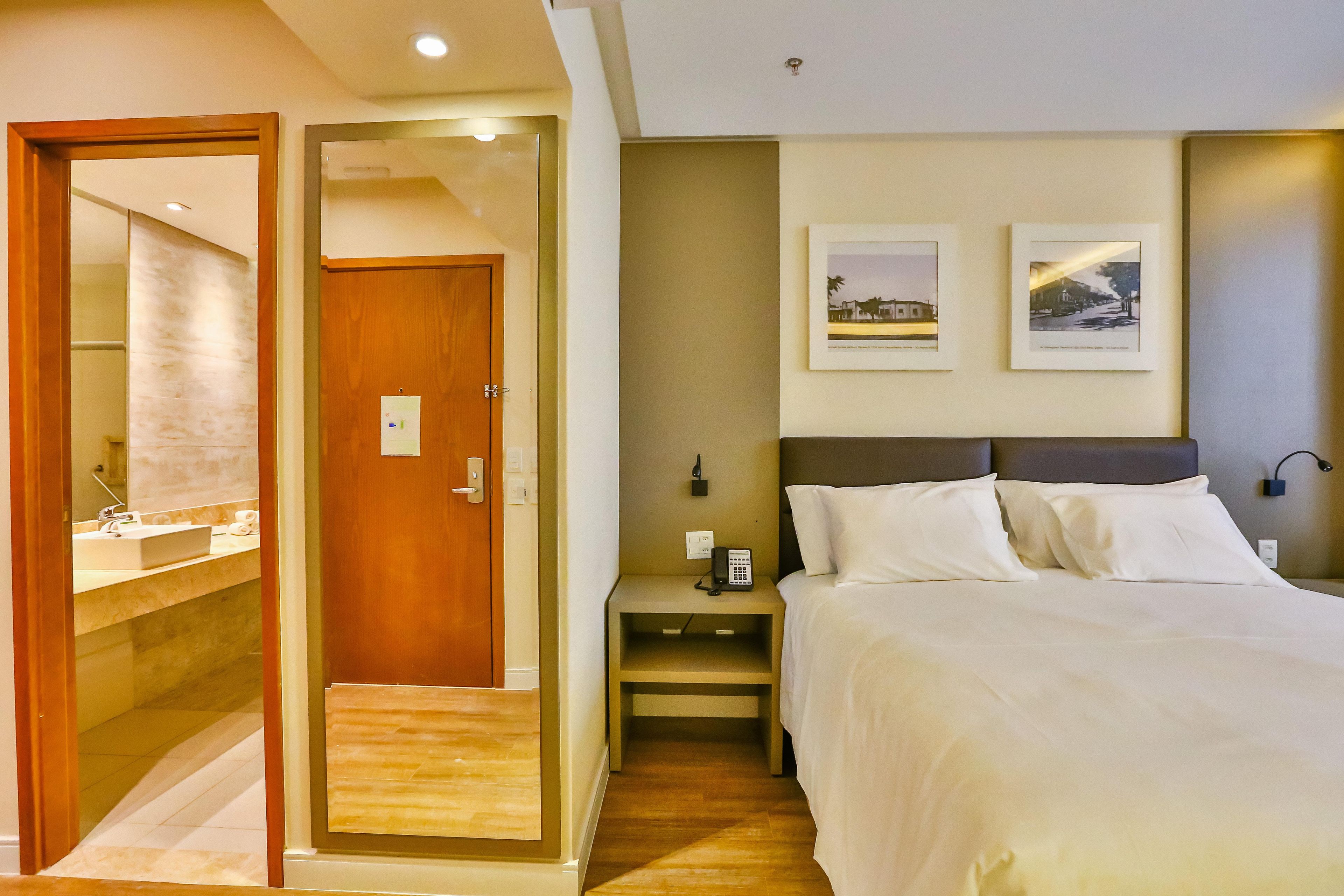 A hotel room with a bed, bedside table, and a mirror.