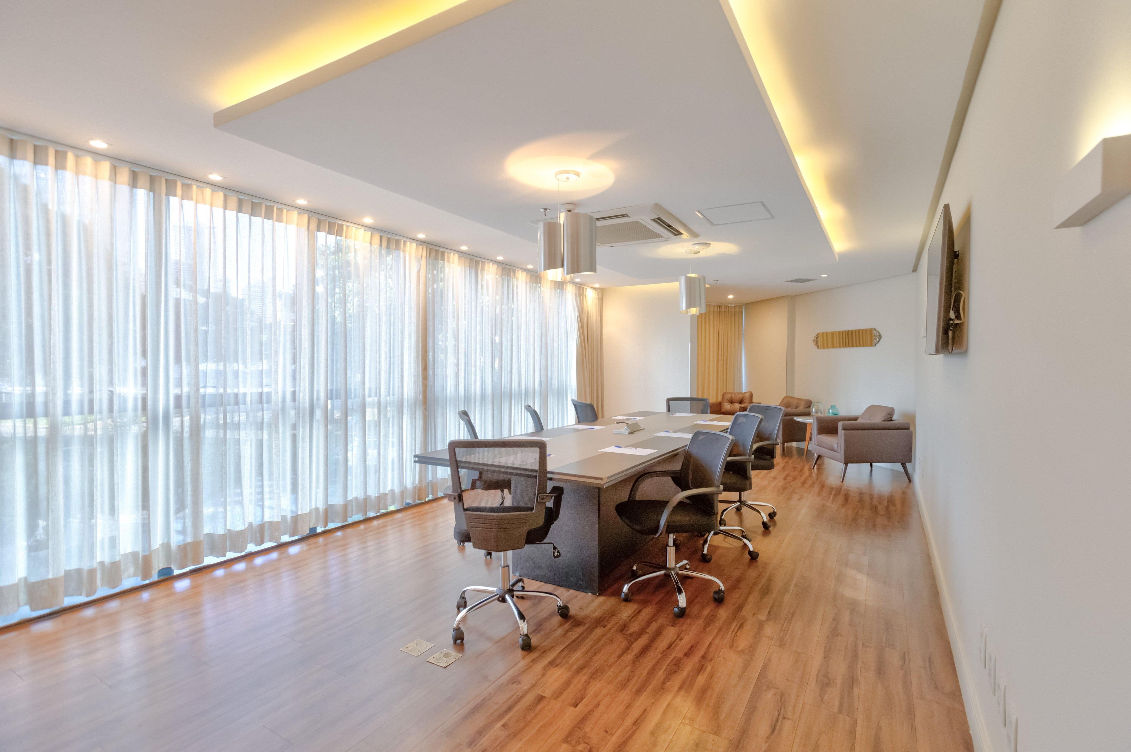 A modern conference room with a long table, chairs, and large windows with sheer curtains.
