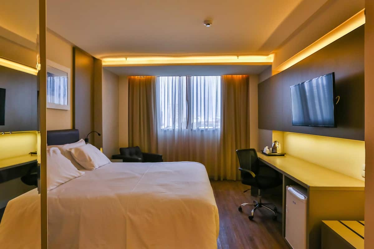 Una habitación de hotel con cama, escritorio, silla, televisión y cortinas.