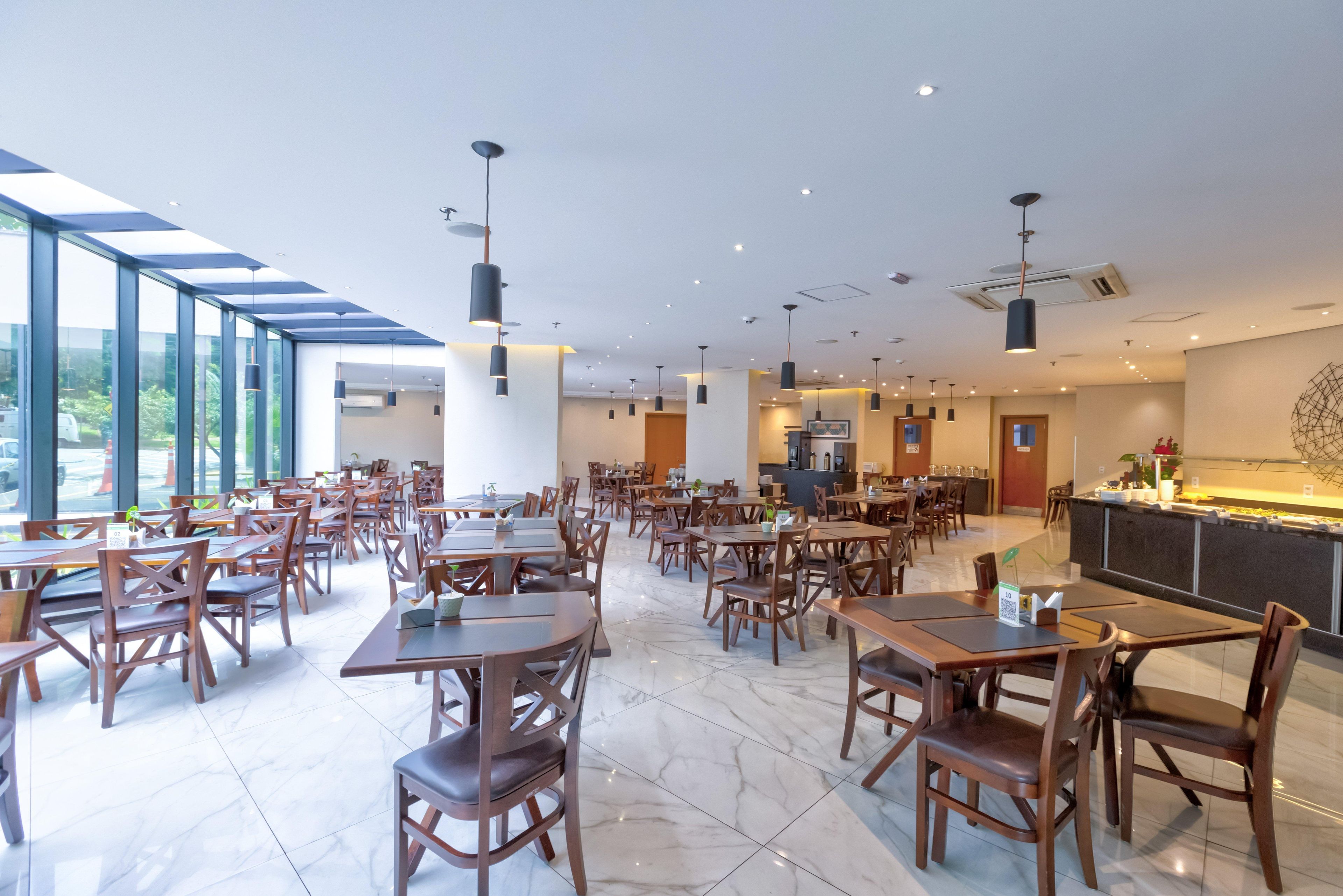 A spacious restaurant with high ceilings, modern pendant lighting, and a large windowed wall providing natural light.
