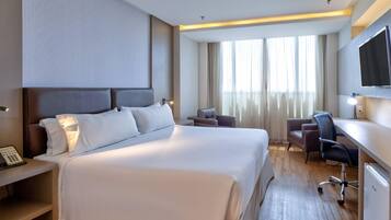 A hotel room with a large bed, a desk with a chair, a television, and a window with curtains.