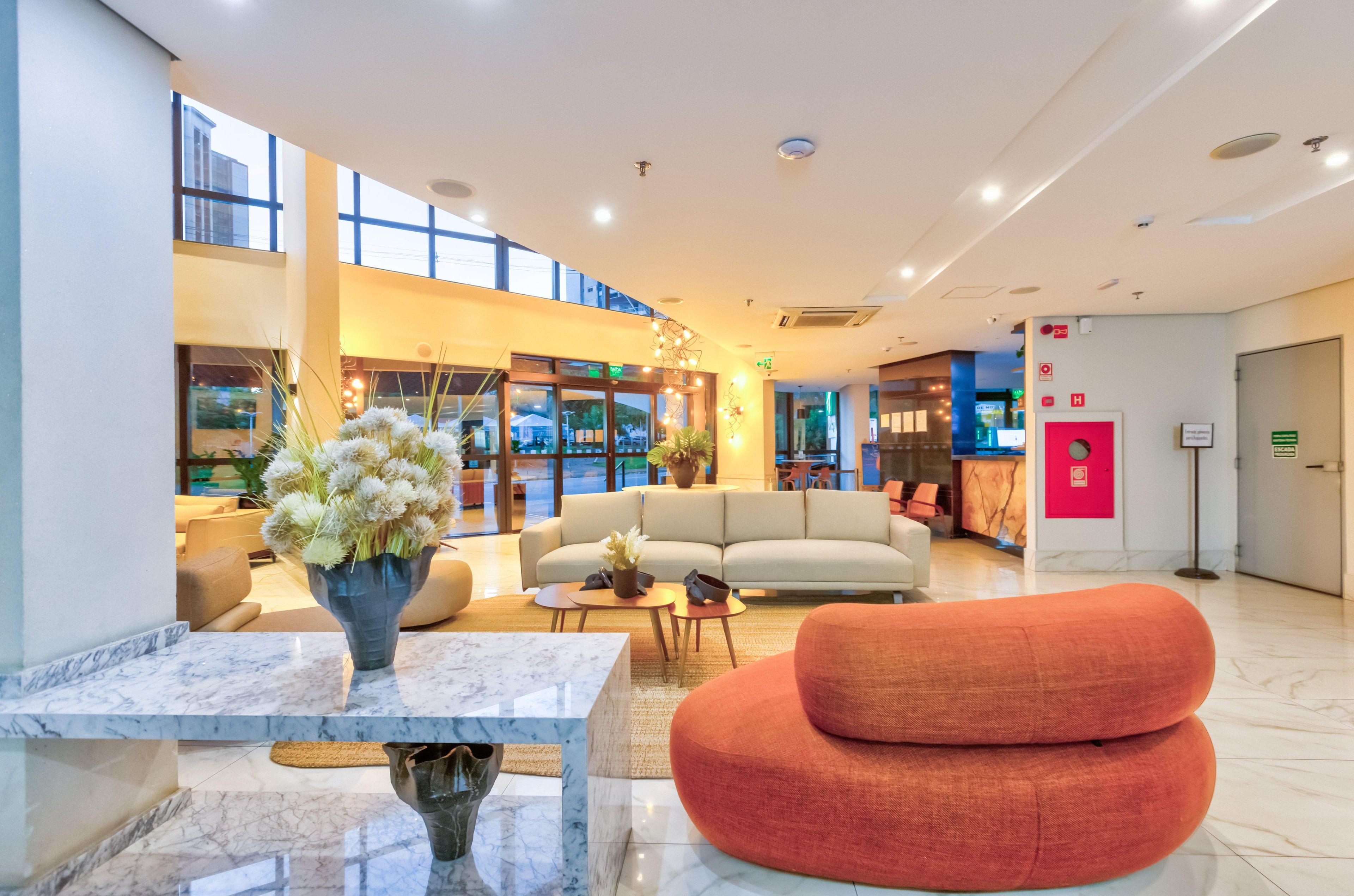 A spacious lobby with a marble reception desk, a sofa, a red chair, and a staircase leading to upper floors.