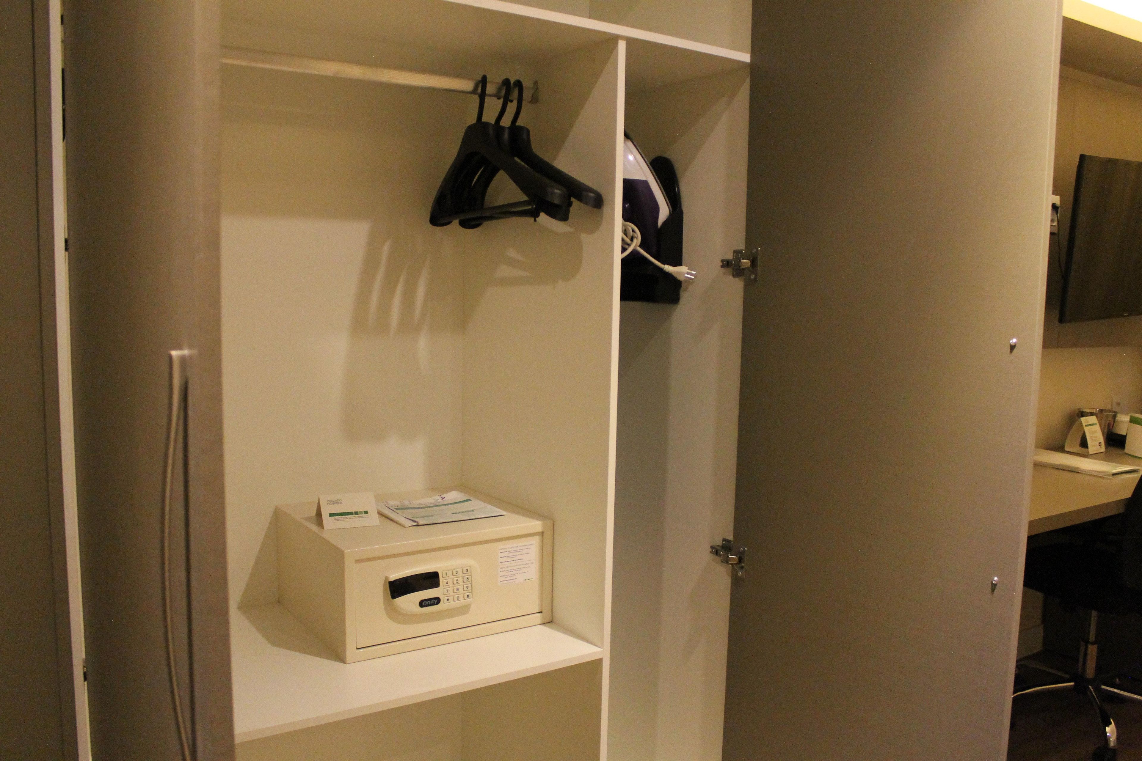 A hotel room with a minibar, a coat rack, and a desk with a computer and a telephone.