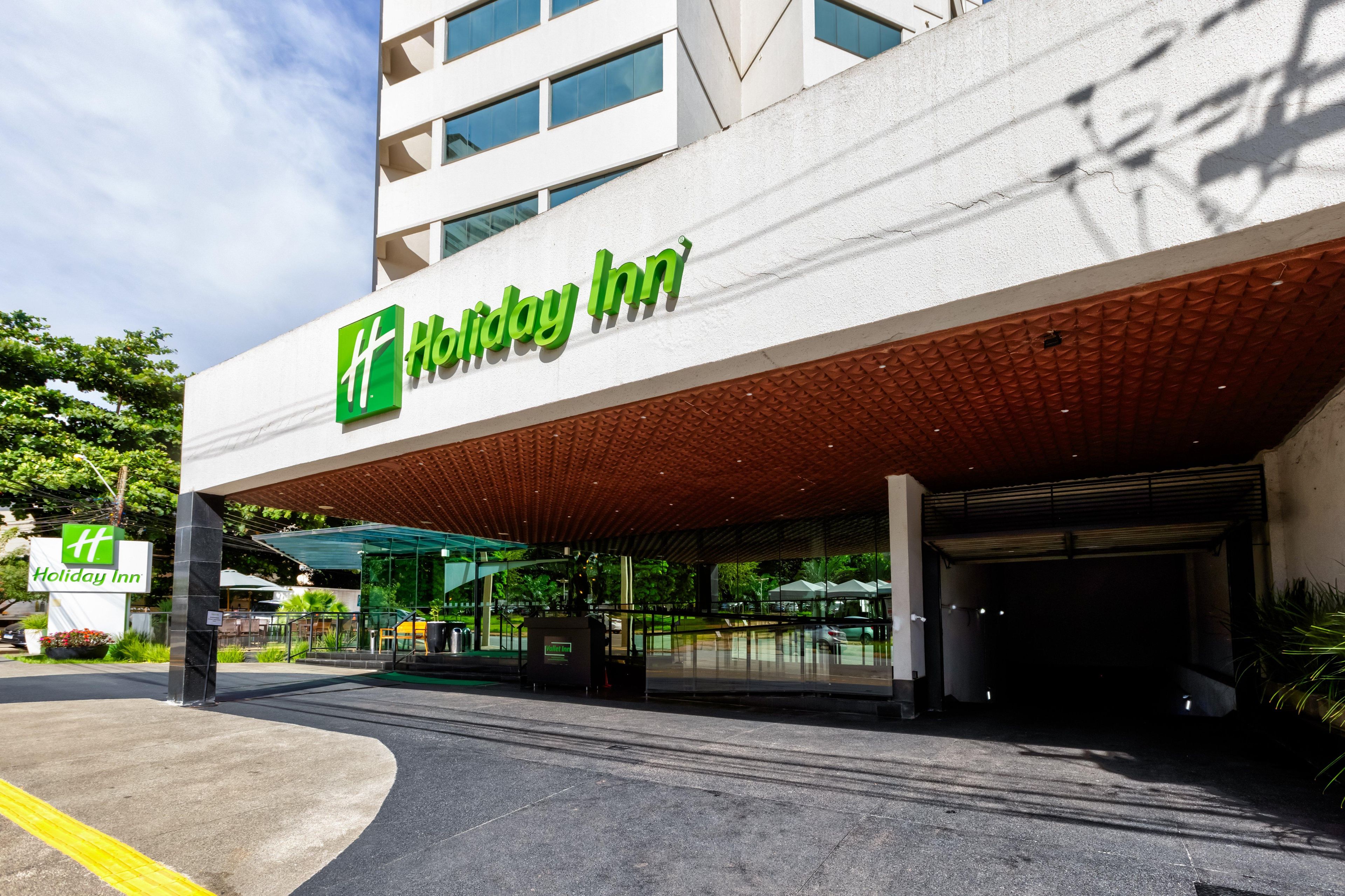 Entrada de un hotel Holiday Inn con diseño moderno, que incluye un corredor cubierto y un cielo despejado.