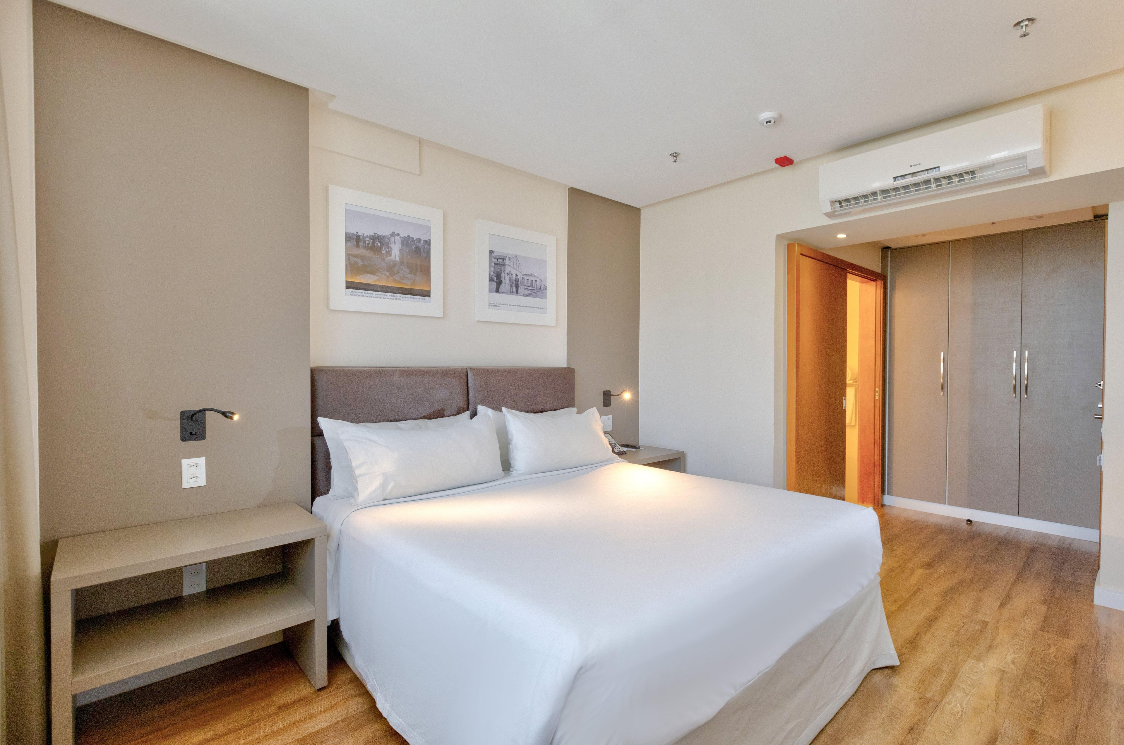 Una habitación de hotel con una cama grande, mesitas de noche, un armario y cuadros en la pared.