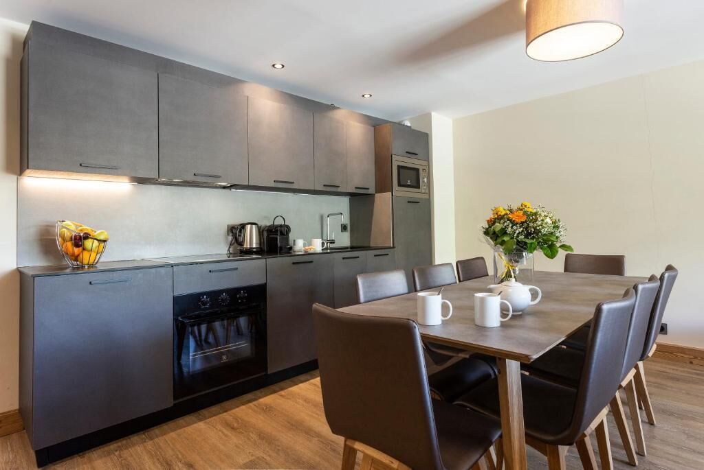 Una cocina moderna con armarios oscuros, horno integrado y un comedor con mesa y sillas.