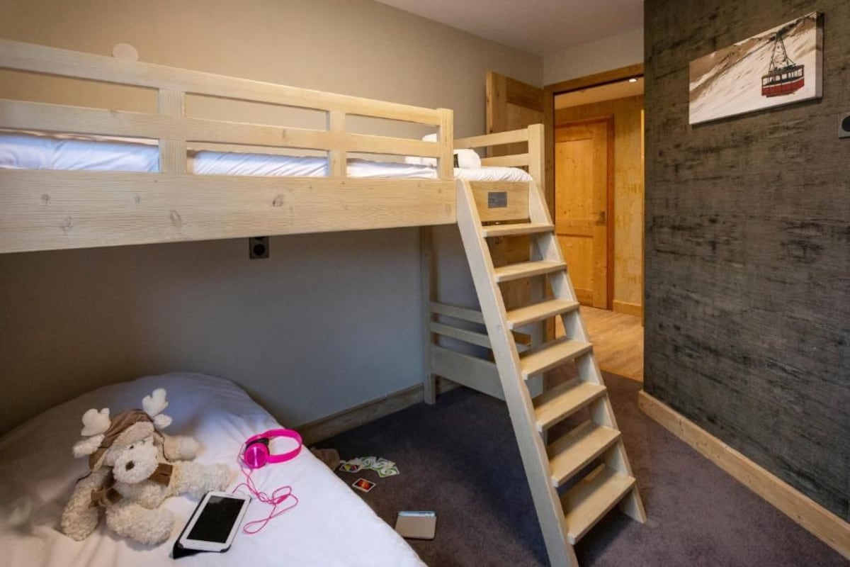 A bunk bed with a wooden ladder, a plush toy, a smartphone, and a wall-mounted picture.