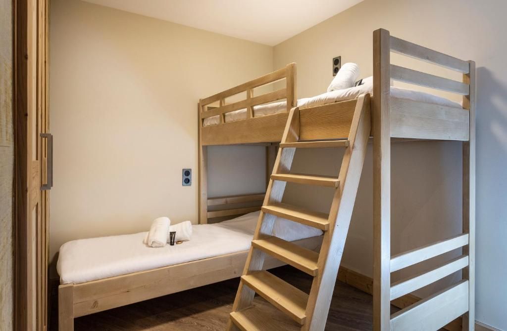 Une chambre avec un lit superposé, une échelle en bois, une petite table de chevet et un luminaire fixé au mur.