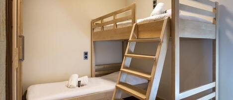 Habitación con literas, una escalera de madera, una mesita de noche pequeña y una lámpara fijada a la pared.