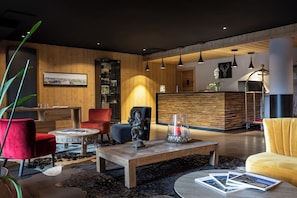 A modern interior with a wooden reception desk, red and yellow seating, and pendant lighting. - Residence Daria-i Nor (Huez)