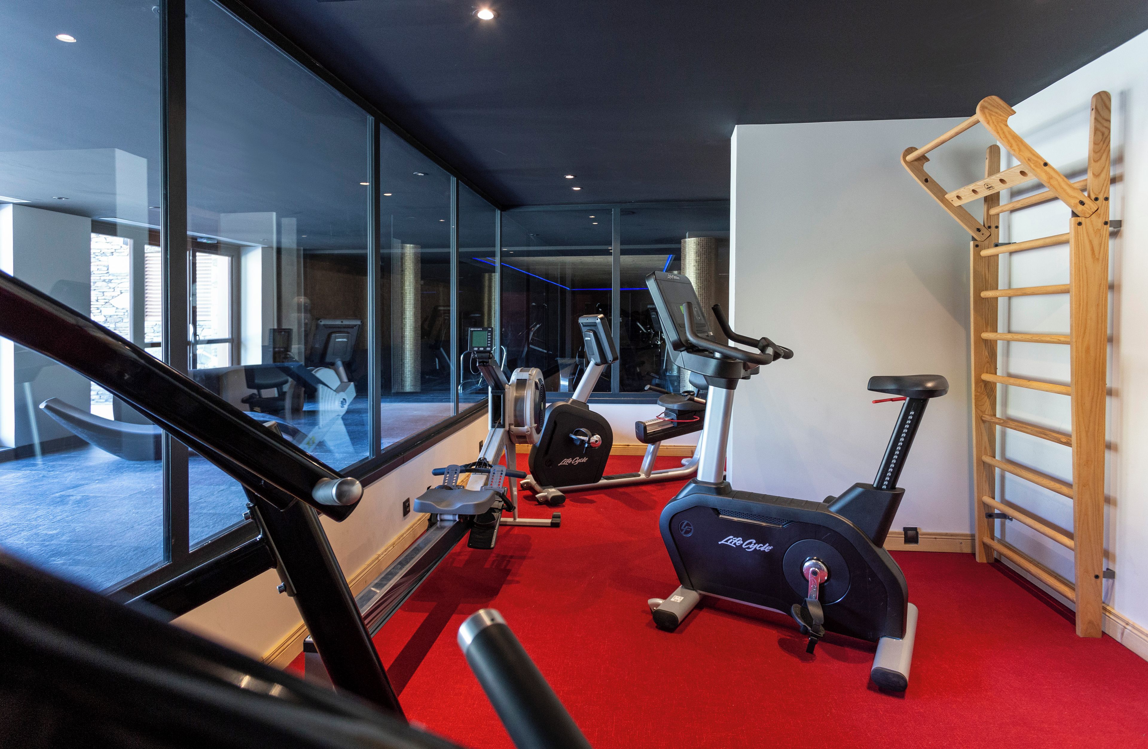 Un gimnasio con equipamiento de ejercicio, una alfombra roja y una escalera de madera.