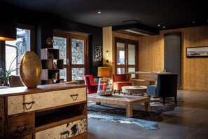 Una sala moderna con una mesa de centro de madera, sillas rojas y negras, un jarrón decorativo grande y una pared de piedra.